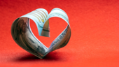 Photo of a $100 bill folded into a heart shape red background Photo of a $100 bill folded into a heart shape red background